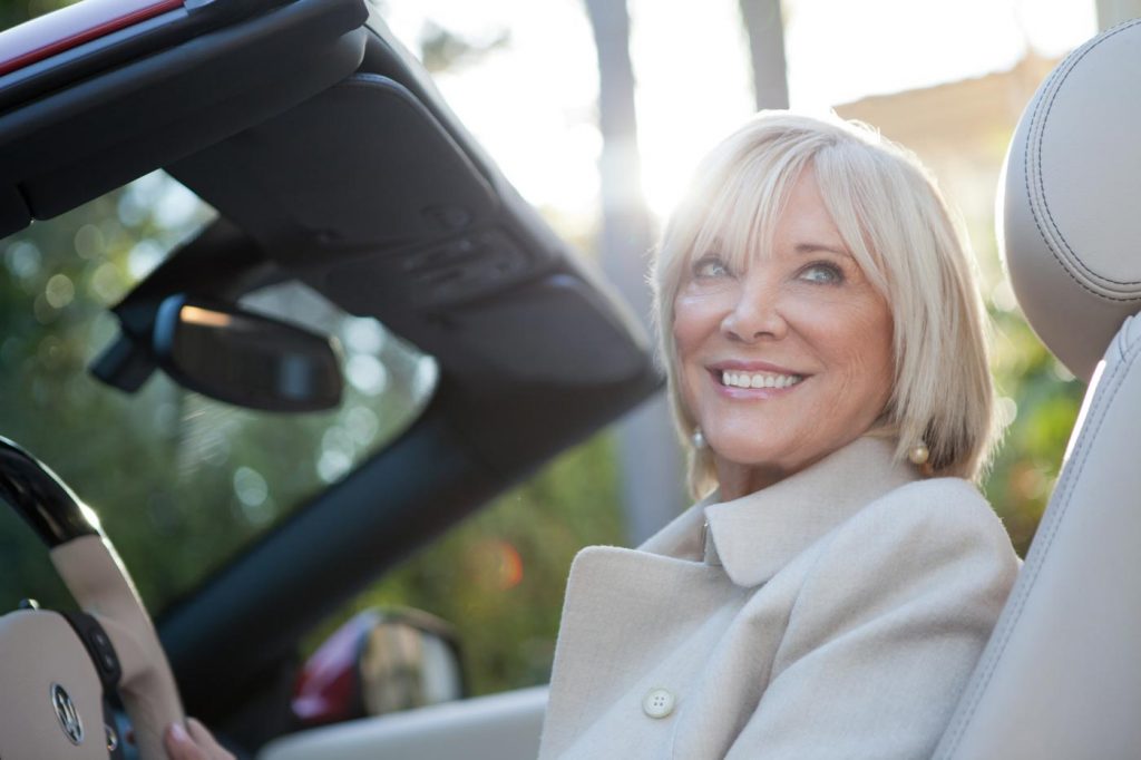 A portrait of Betty Graham for Coldwell Banker Previews, a classy older lady with silver hair smiling off camera sitting in the driver seat of a Maserati. Photo taken by Los Angeles corporate photographer Nick Reid.