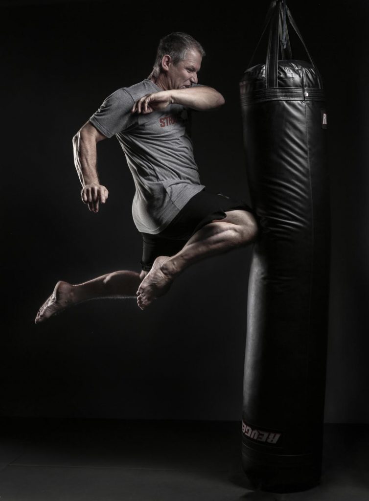 John Whitman flying through the air kneeing a punching bag by Los Angeles sports portrait photographer Nick Reid.