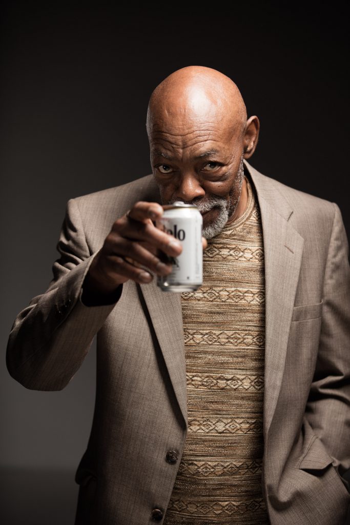 Ralph Thompson in a suit jacked toasting the Los Angeles portrait photographer with a beer and a smile