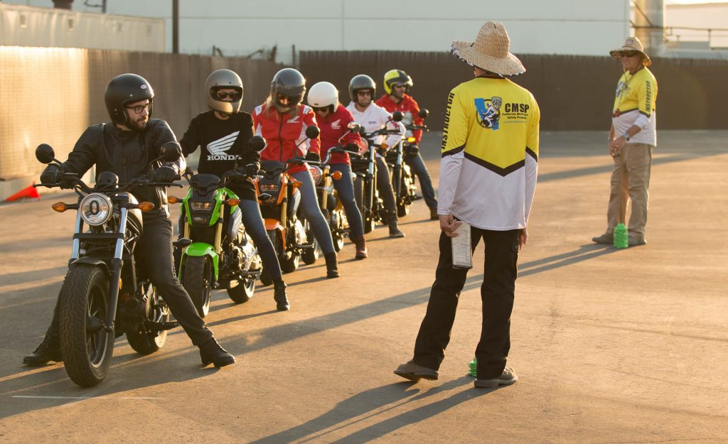 A group of students on Honda motorcycles line up and listen to their instructor.